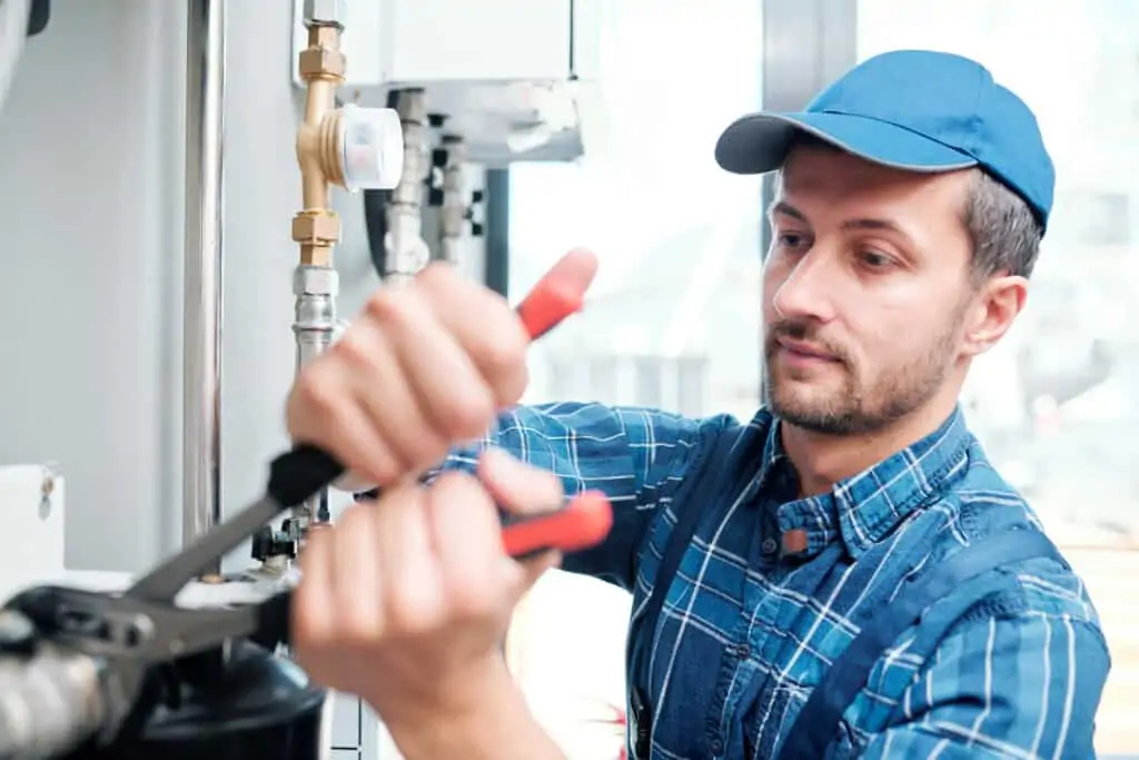 Contemporary young mechanic from household maintenance service repairing pipe in the kitchen of client